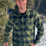 A man wearing a black and olive buffalo check flannel shirt with two flap breast pockets and a two button cuff.