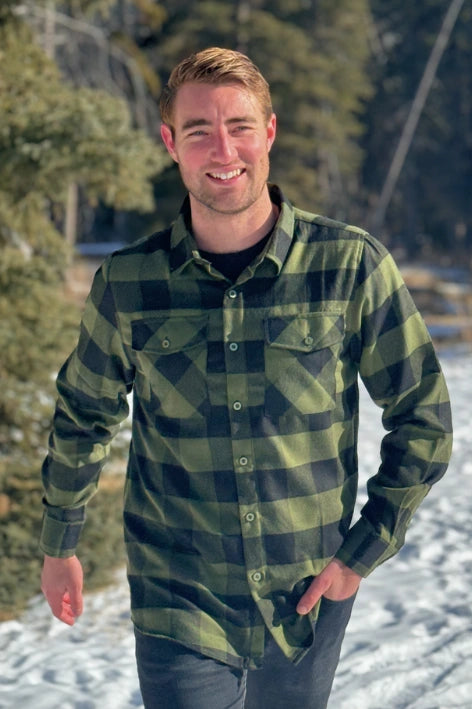 A man wearing a black and olive buffalo check flannel shirt with two flap breast pockets and a two button cuff.
