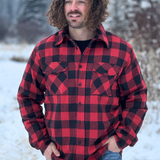 A man wearing a red and black checkered padded flannel jacket, standing outdoors in a snowy environment.