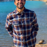Man wearing a plaid flannel shirt standing by a river with trees in the background in Banff National Park
