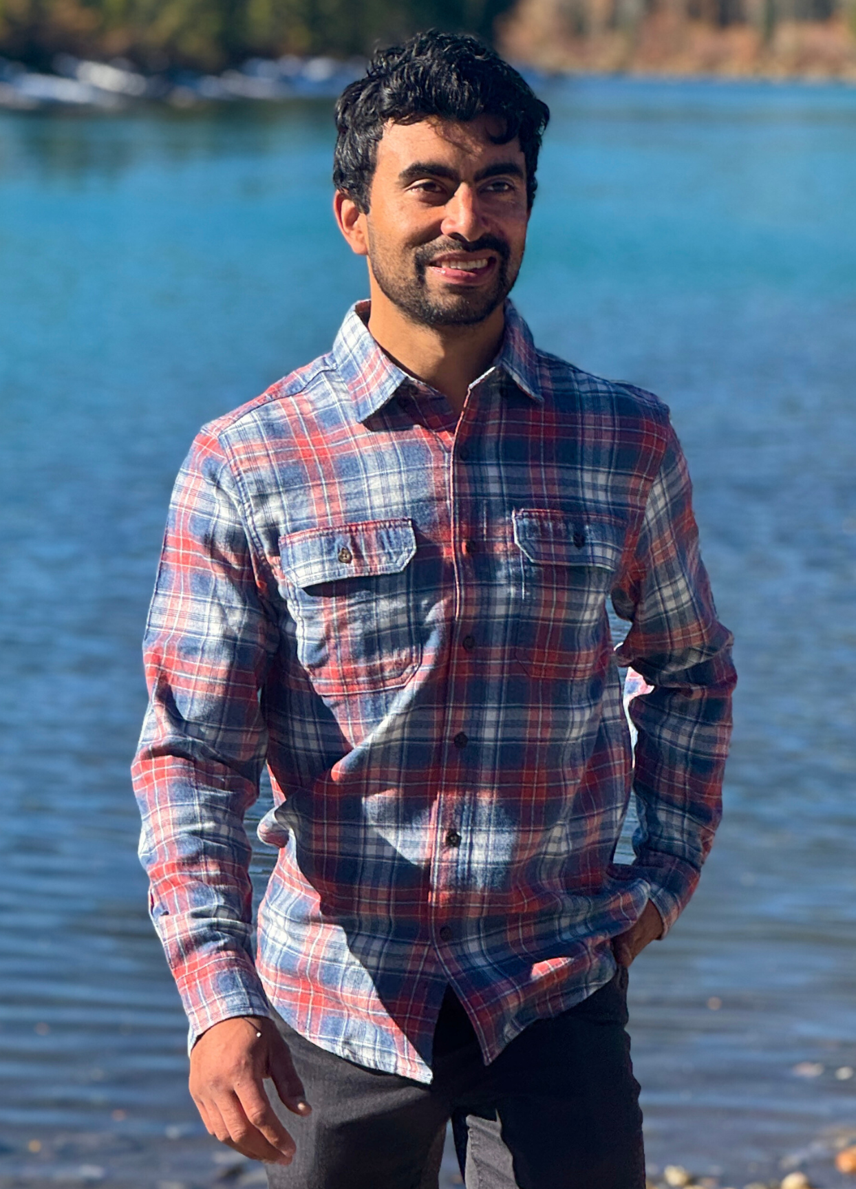 Man wearing a plaid flannel shirt standing by a body of water in Banff National Park