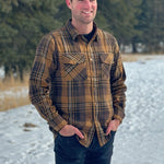 A man wearing a mocha brown flannel shirt with two flap breast pockets and a shirt tail hemline, standing outdoors.