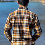 Man wearing a plaid flannel shirt by a river with trees in the background in Banff National Park