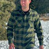 A man wearing a black and olive buffalo check flannel shirt with two flap breast pockets and a two button cuff.