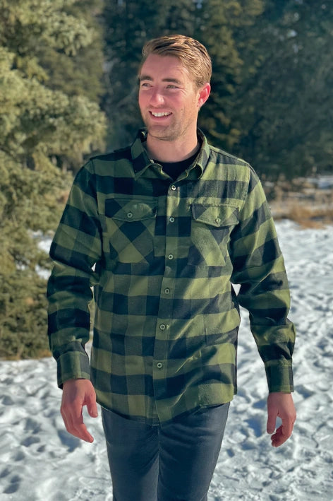 A man wearing a black and olive buffalo check flannel shirt with two flap breast pockets and a two button cuff.