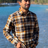 Man wearing a plaid flannel shirt standing by a river with trees in the background in Banff National Park