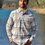Man wearing a plaid flannel shirt standing by a river with mountains in the background in Banff National Park