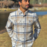 Man wearing a plaid flannel shirt standing outdoors with a river and trees in the background in Banff National Park
