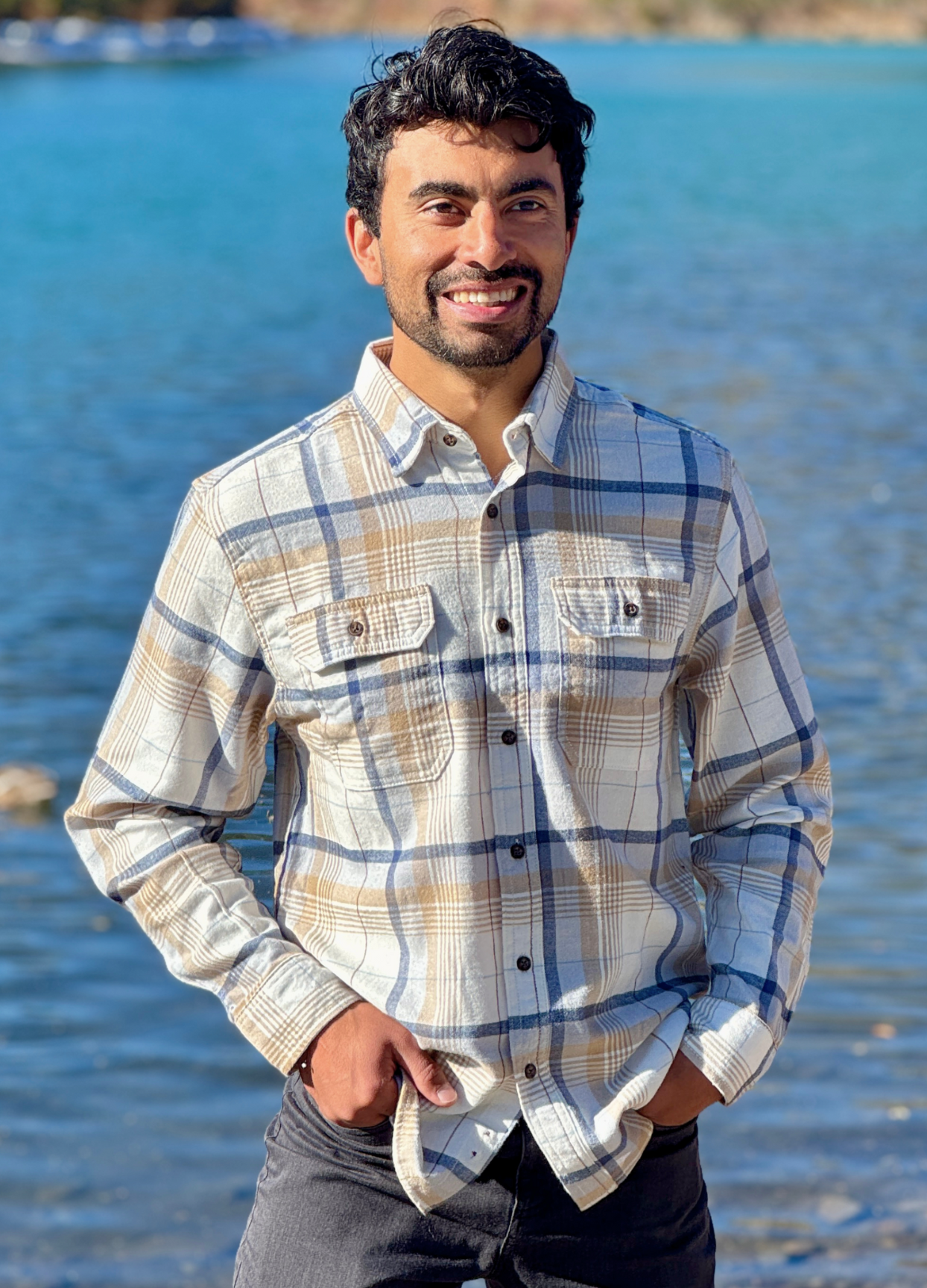 Man wearing a plaid flannel shirt standing by a body of water in Banff National Park
