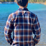 Person wearing a plaid flannel shirt standing by a river with mountains in the background in Banff National Park