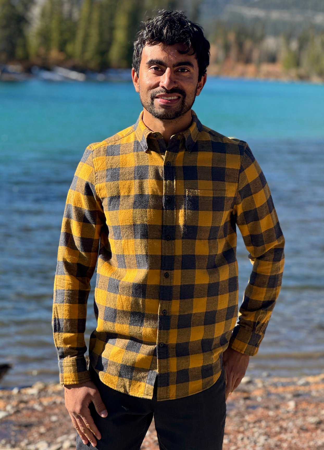Man wearing a gold and grey checkered shirt standing by a river in Banff National Park.