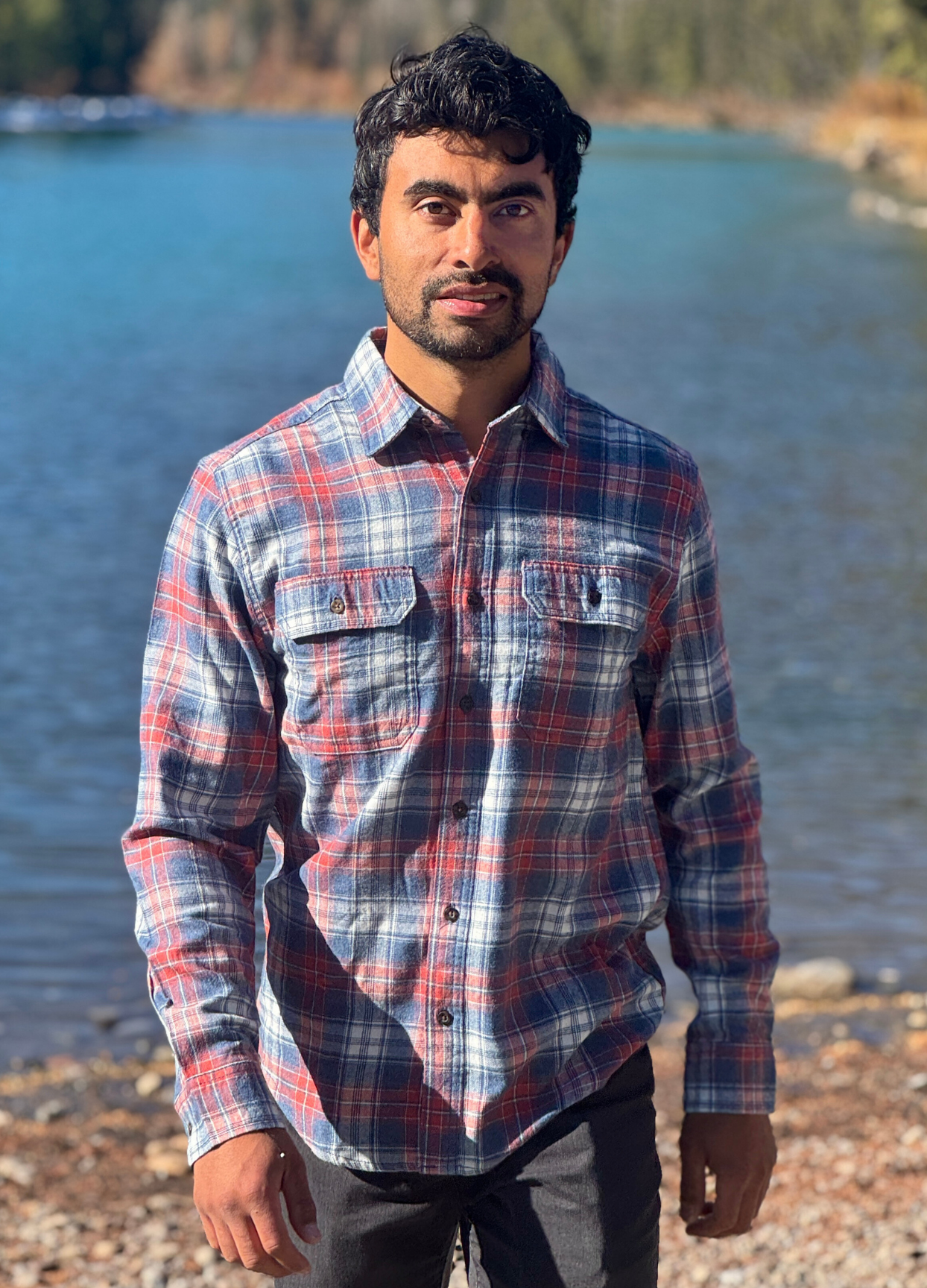 Man wearing a plaid flannel shirt standing by a river in Banff National Park