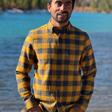 Man wearing a gold and grey plaid flannel shirt standing by a river with mountains in the background in Banff National Park