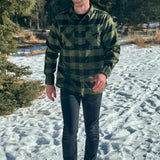 A man wearing a black and olive buffalo check flannel shirt with two flap breast pockets and a two button cuff.
