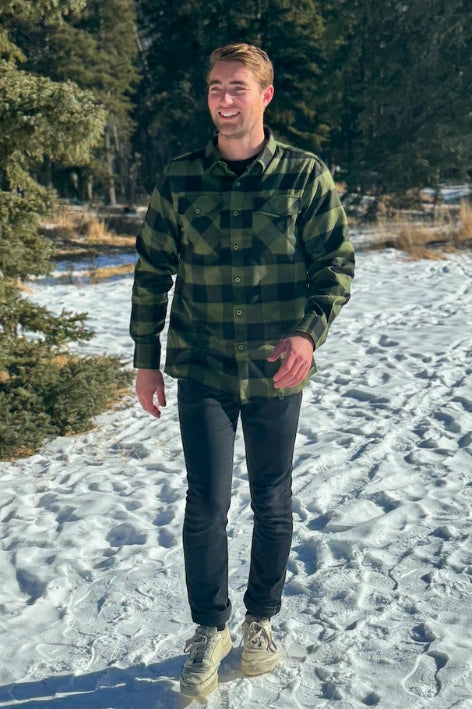 A man wearing a black and olive buffalo check flannel shirt with two flap breast pockets and a two button cuff.