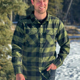 A man wearing a black and olive buffalo check flannel shirt with two flap breast pockets and a two button cuff.