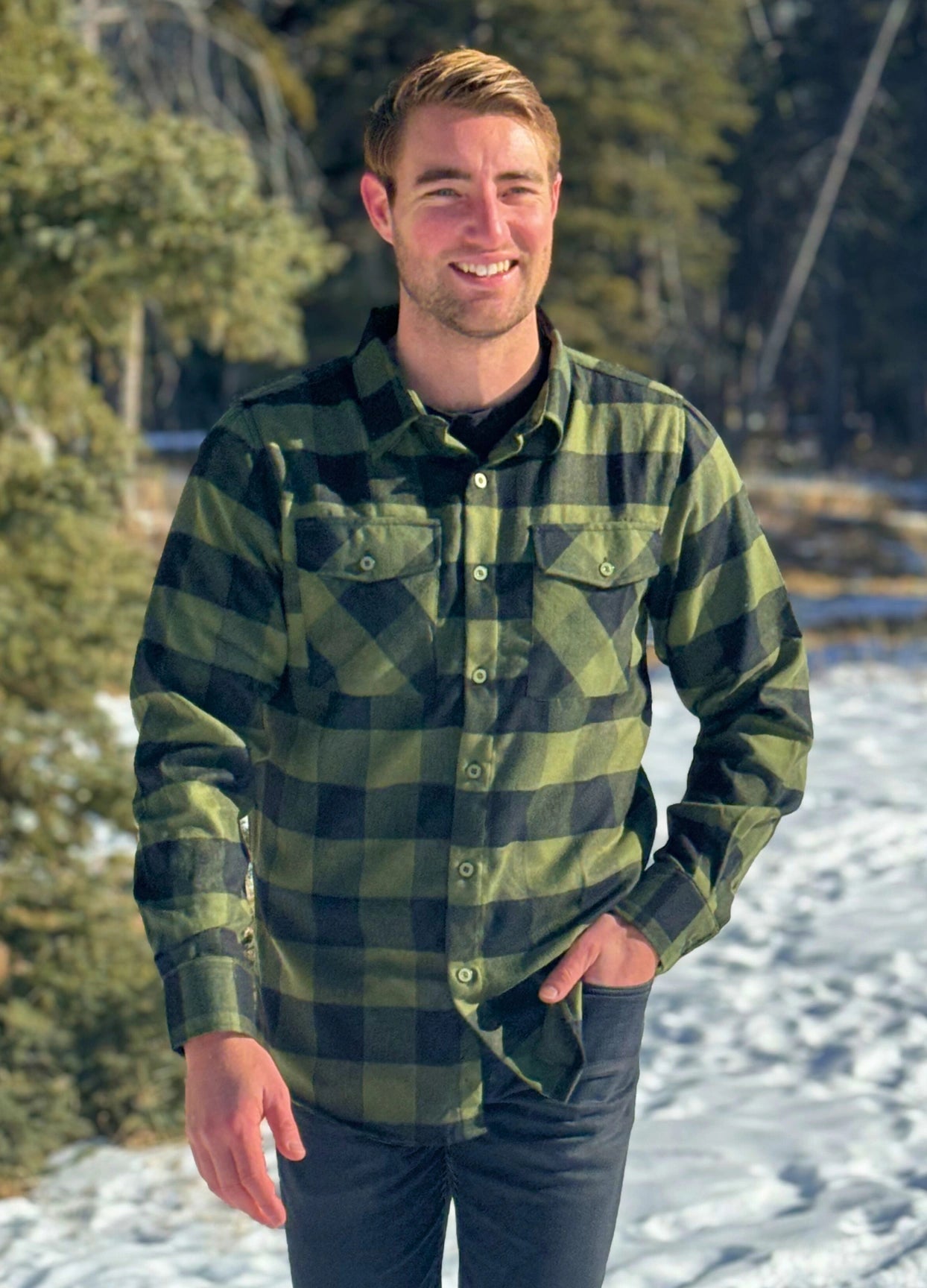 A man wearing a black and olive buffalo check flannel shirt with two flap breast pockets and a two button cuff.