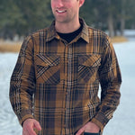 A man wearing a mocha brown flannel shirt with two flap breast pockets and a shirt tail hemline, standing outdoors.