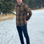 A man wearing a mocha brown flannel shirt with two flap breast pockets and a shirt tail hemline, standing outdoors.