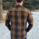 Back view of a man wearing a mocha brown flannel shirt with two flap breast pockets and a shirt tail hemline, standing outdoors.