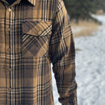 A man wearing a mocha brown flannel shirt with two flap breast pockets and a shirt tail hemline, standing outdoors.