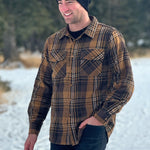 A man wearing a mocha brown flannel shirt with two flap breast pockets and a shirt tail hemline, standing outdoors.