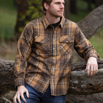 A man wearing a mocha brown plaid flannel shirt with two flap breast pockets and two button cuffs, standing next to a tree.