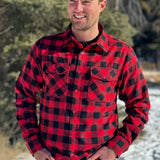 A man wearing a red and black buffalo check flannel shirt with two flap breast pockets and a button cuff, standing outdoors.