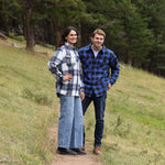 A man wearing a royal blue and black buffalo check padded flannel camping outdoor jacket with jeans.