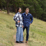 A man wearing a royal blue and black buffalo check padded flannel camping outdoor jacket with jeans.
