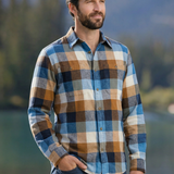 Man wearing a flannel shirt standing outdoors with mountains and water in the background