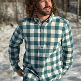A man standing outdoors wearing a teal buffalo check flannel shirt with long sleeves, button-up collar, and a single breast pocket.