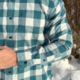 Close up of a man standing outdoors wearing a teal buffalo check flannel shirt with long sleeves, button-up collar, and a single breast pocket.