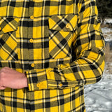 A man wearing a long-sleeved yellow and black flannel plaid shirt with two flap breast pockets and a button cuff.