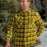 A man wearing a long-sleeved yellow and black flannel plaid shirt with two flap breast pockets and a button cuff.