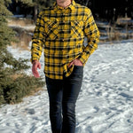 A man wearing a long-sleeved yellow and black flannel plaid shirt with two flap breast pockets and a button cuff.