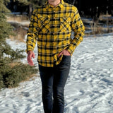 A man wearing a long-sleeved yellow and black flannel plaid shirt with two flap breast pockets and a button cuff.