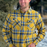 A man wearing a yellow and blue large plaid long-sleeved shirt standing outdoors.