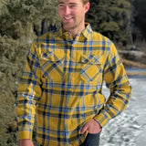 A man wearing a yellow and blue large plaid long-sleeved shirt standing outdoors.