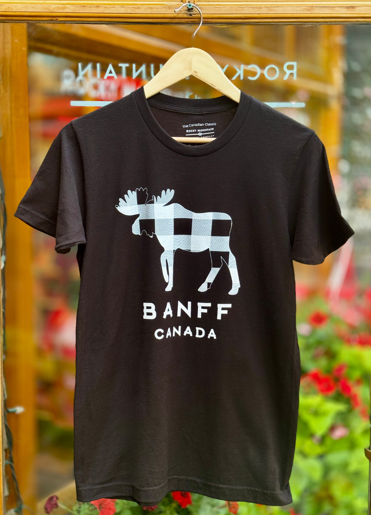 Black t-shirt with moose graphic and 'Banff Canada' text on a hanger against a blurred background.