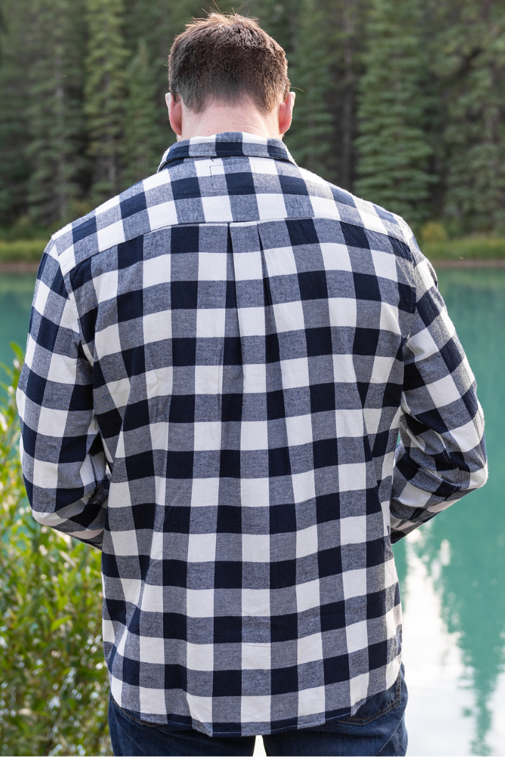 Back view of a man wearing a navy and cream check flannel shirt with a button-down collar, single breast pocket, and long sleeves.