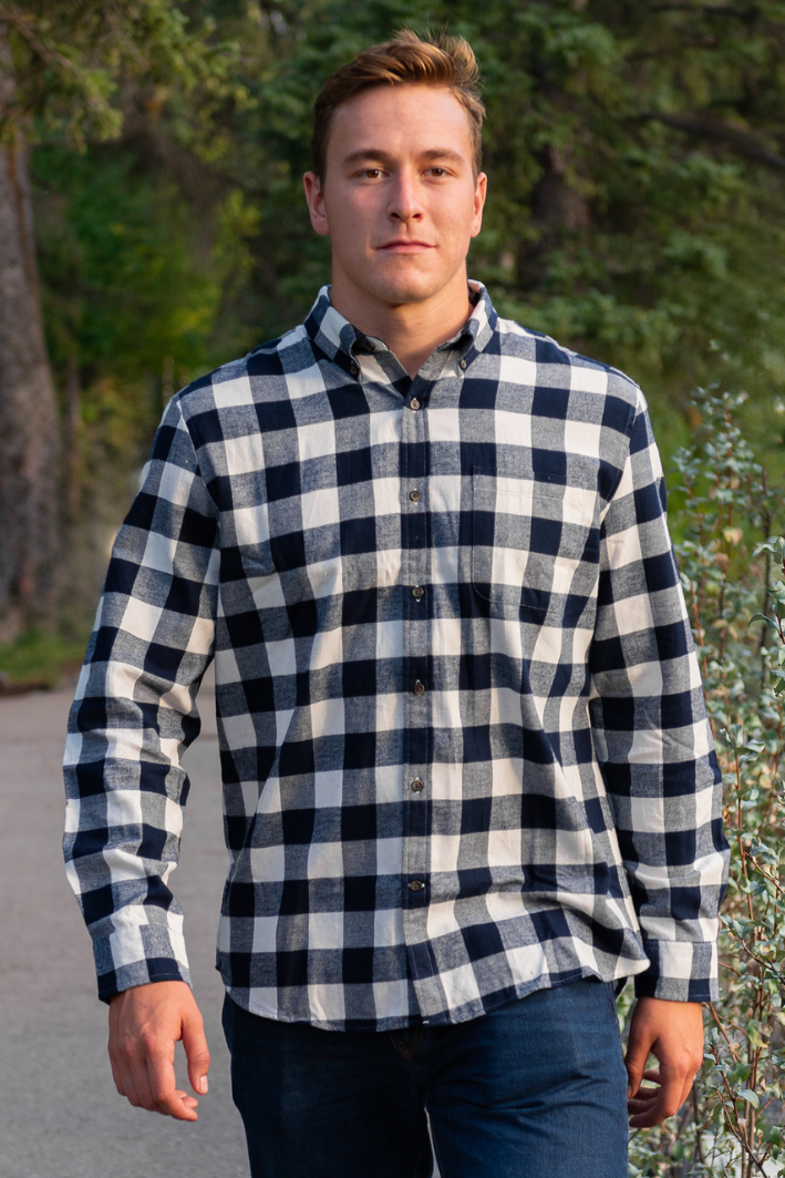 A man wearing a navy and cream check flannel shirt with a button-down collar, single breast pocket, and long sleeves.