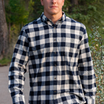 A man wearing a navy and cream check flannel shirt with a button-down collar, single breast pocket, and long sleeves.