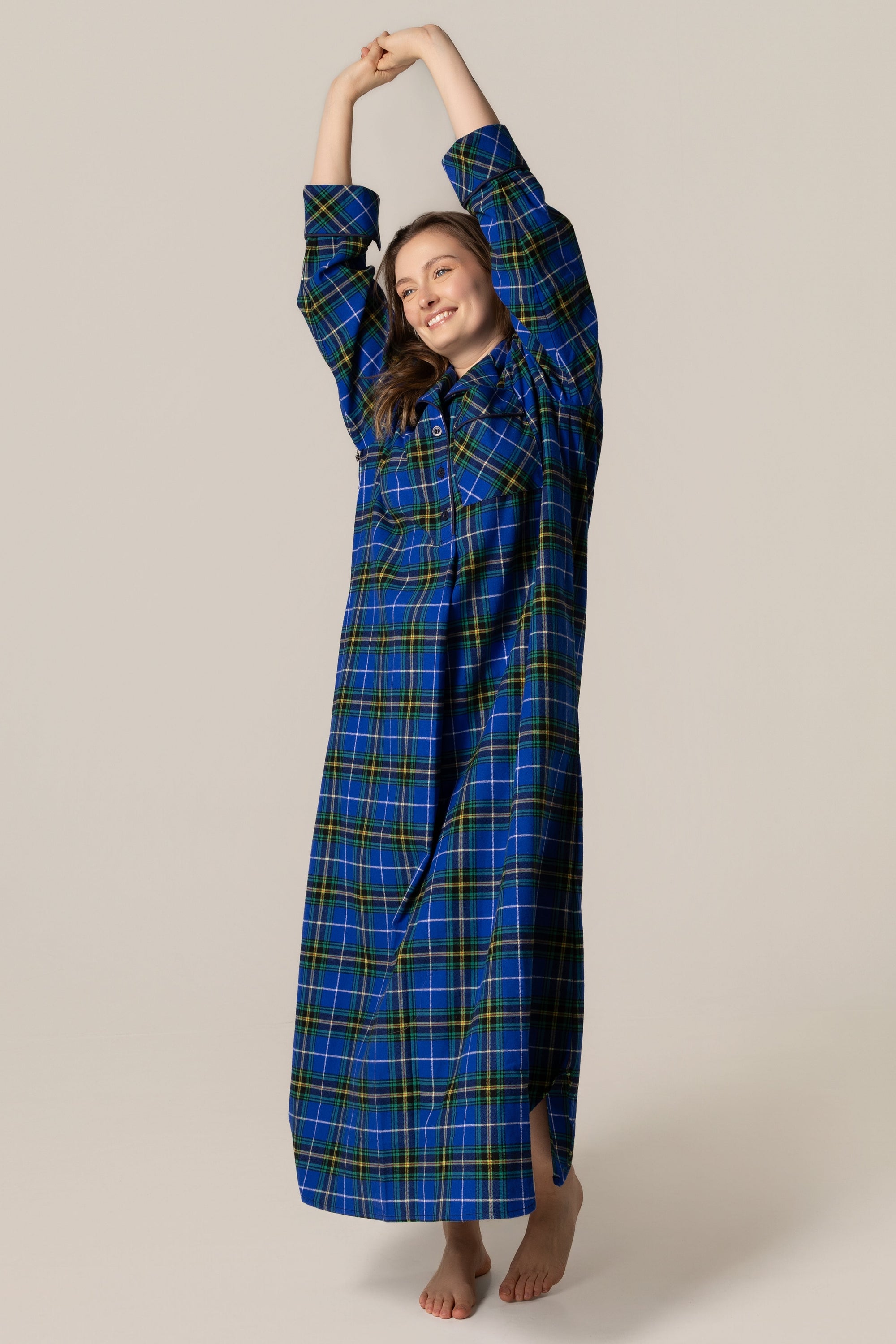 Woman wearing a blue plaid nightgown stretching her arms above her head on a beige background