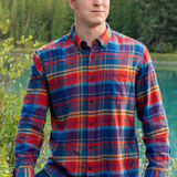 A man standing outdoors wearing a long-sleeved orange, red, and blue plaid flannel shirt with a collar.