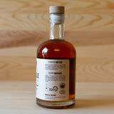 Back label of a bottle of Rebelle brand maple syrup with a wooden cap, placed on a wooden surface.