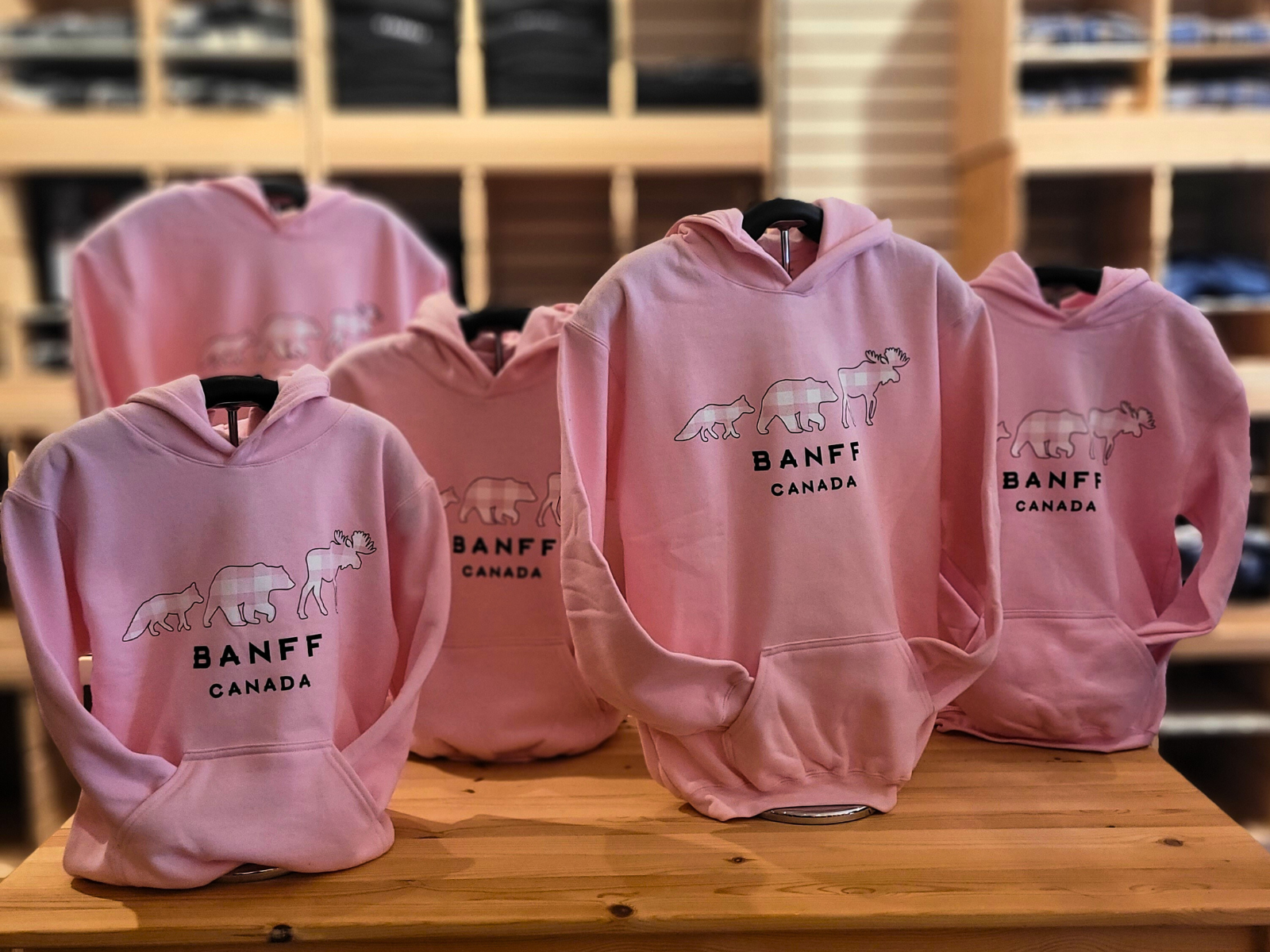 Pink hoodies with 'Banff Canada' logo on a wooden table