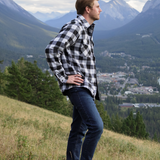 Man standing in front of mountains. He is turned to the side with his hands on his hips. He is wearing our padded flannel camping jacket in black and white buffalo check.