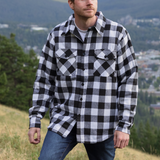 A man wearing a long-sleeved black and white checkered flannel padded jacket with a collar, button cuffs, and a shirttail hemline, standing outdoors.