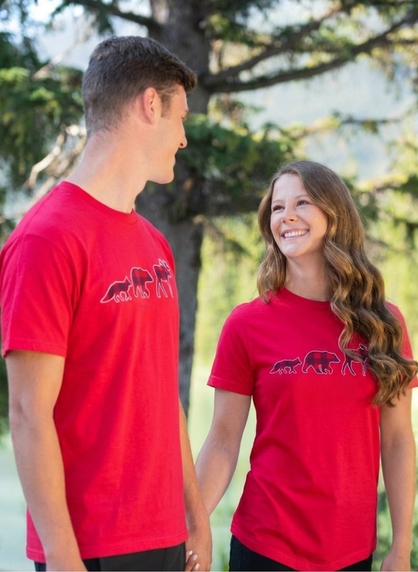 Two people wearing red t-shirts with moose, bear and fox graphic outdoors, holding hands.